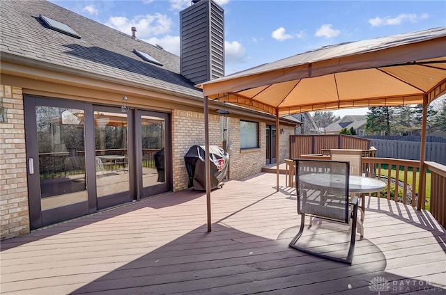 deck featuring a gazebo, outdoor dining area, a grill, and fence