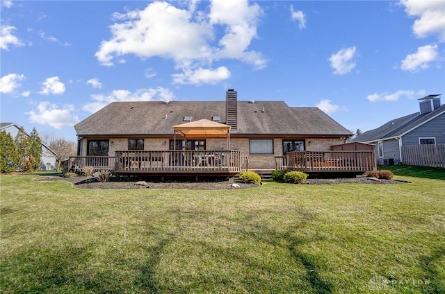 back of house featuring brick siding, a chimney, a wooden deck, and a yard