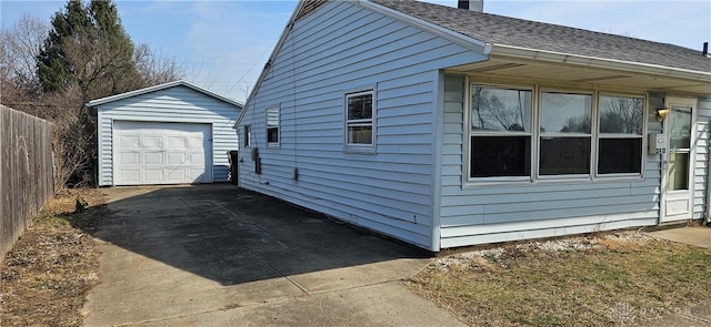 view of side of property featuring an outbuilding, fence, roof with shingles, concrete driveway, and a detached garage