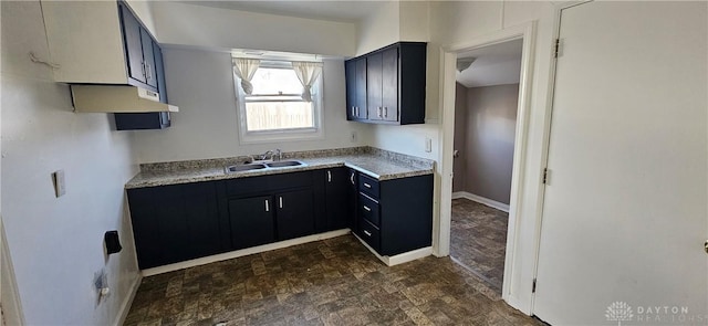 kitchen featuring light countertops, stone finish floor, baseboards, and a sink