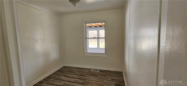 spare room with dark wood-style floors, visible vents, baseboards, and ornamental molding