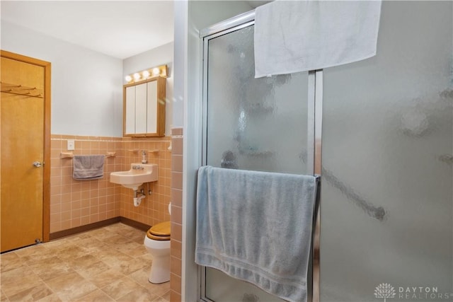 bathroom with toilet, wainscoting, a stall shower, tile walls, and a sink