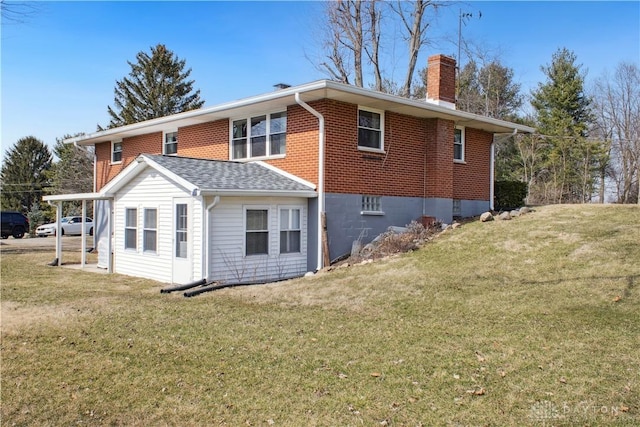 rear view of property featuring brick siding, a lawn, and a chimney