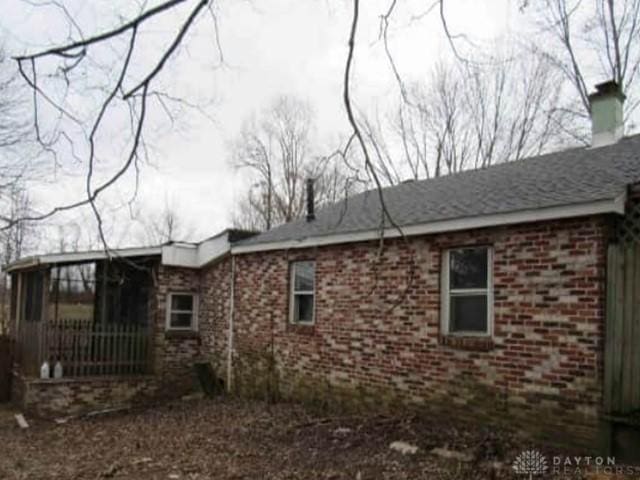 view of side of home with brick siding, a chimney, and a sunroom