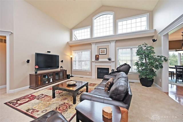 carpeted living area with a glass covered fireplace, baseboards, a wealth of natural light, and high vaulted ceiling