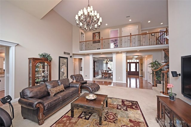 living area featuring stairs, an inviting chandelier, decorative columns, and visible vents