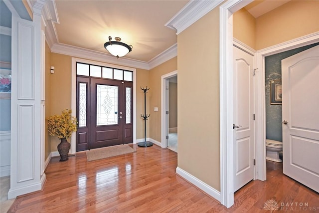 entrance foyer with ornate columns, baseboards, crown molding, and light wood-style floors