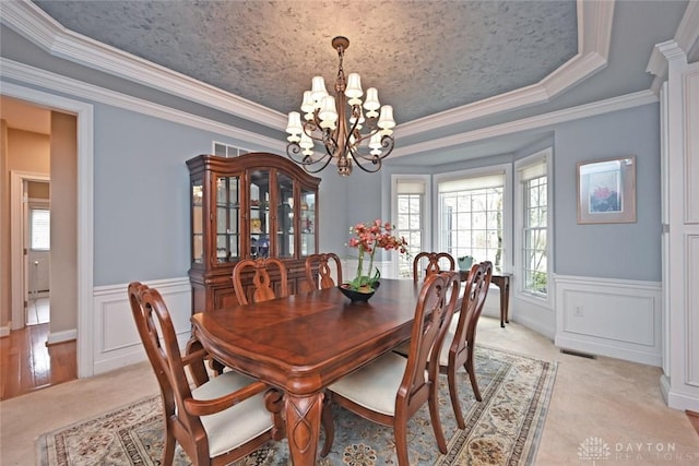 dining area with a tray ceiling, a notable chandelier, visible vents, and wainscoting