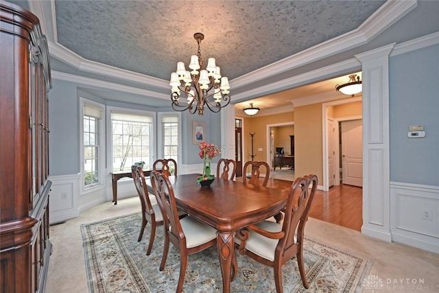 dining space with a raised ceiling, an inviting chandelier, wainscoting, and a decorative wall