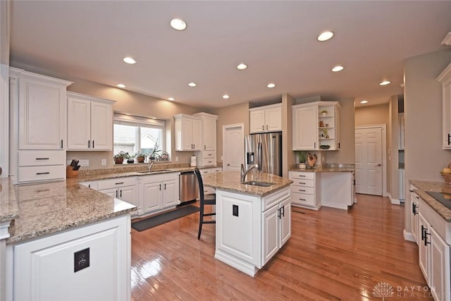 kitchen with white cabinetry, stainless steel appliances, an island with sink, and open shelves