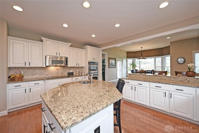 kitchen with a kitchen island with sink, a sink, appliances with stainless steel finishes, a kitchen breakfast bar, and light wood-type flooring