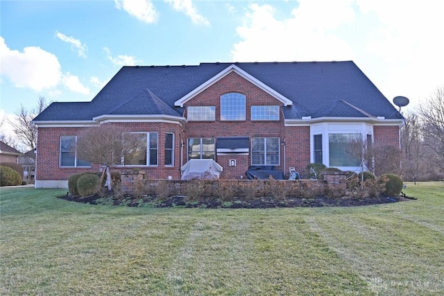 back of house with brick siding, a shingled roof, and a yard