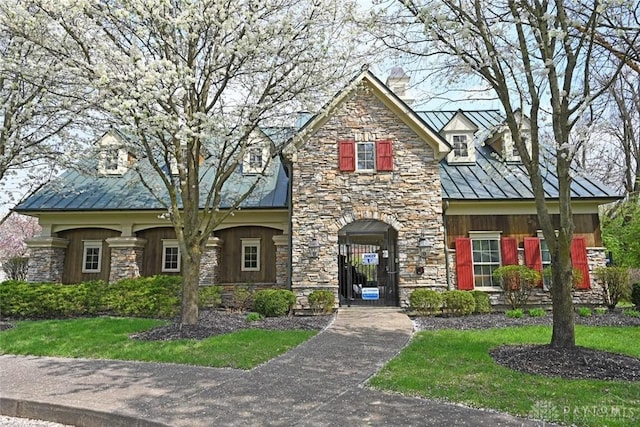 view of front of house featuring a chimney, stone siding, metal roof, and a standing seam roof