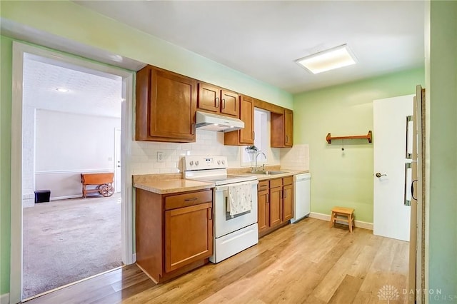 kitchen with tasteful backsplash, under cabinet range hood, light countertops, white appliances, and a sink