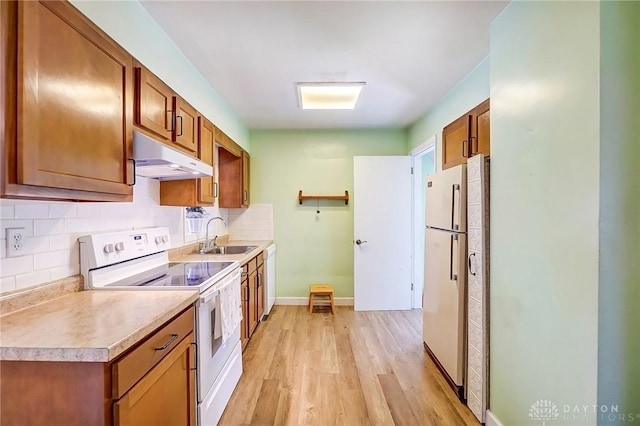 kitchen with white appliances, light wood-style flooring, a sink, under cabinet range hood, and brown cabinets