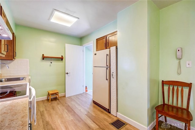 kitchen featuring visible vents, light wood-style flooring, a sink, backsplash, and white appliances