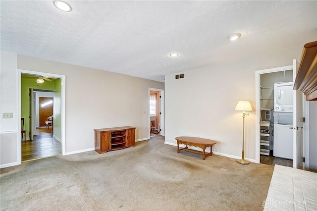 living room with visible vents, a textured ceiling, stacked washing maching and dryer, carpet flooring, and ceiling fan