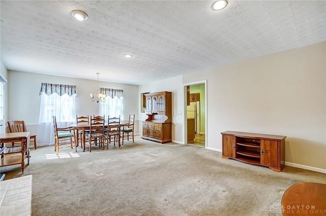 dining room featuring a textured ceiling, light colored carpet, baseboards, and a chandelier