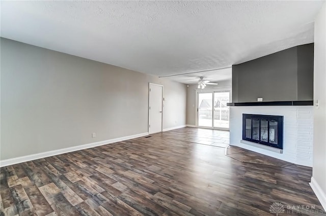 unfurnished living room featuring baseboards, dark wood-type flooring, ceiling fan, and a textured ceiling