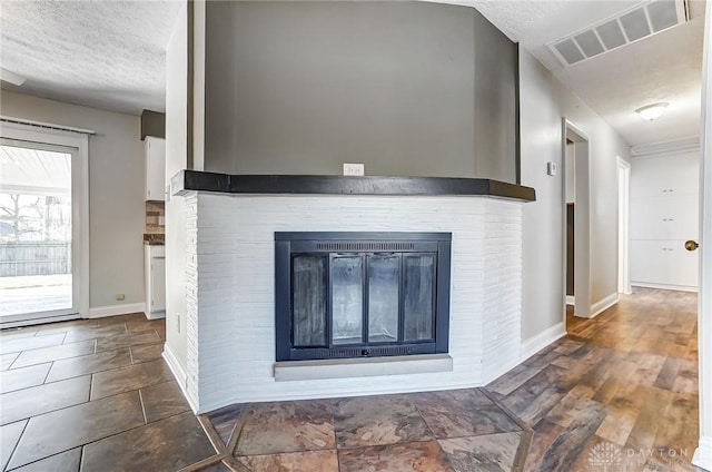 details featuring visible vents, a textured ceiling, wood finished floors, a fireplace, and baseboards