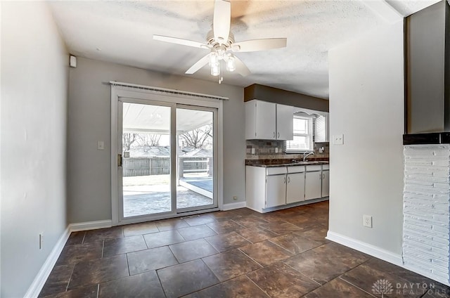 kitchen with tasteful backsplash, dark countertops, white cabinetry, baseboards, and ceiling fan