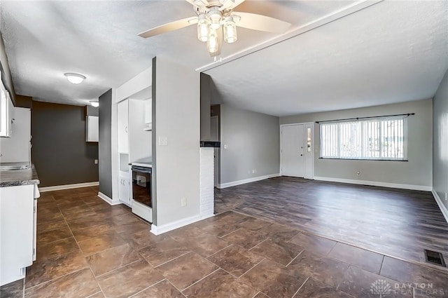 unfurnished living room with a sink, visible vents, baseboards, and ceiling fan