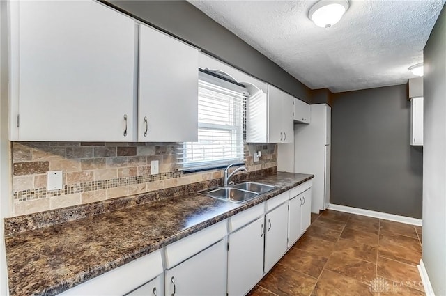 kitchen featuring a sink, backsplash, dark countertops, white cabinetry, and baseboards