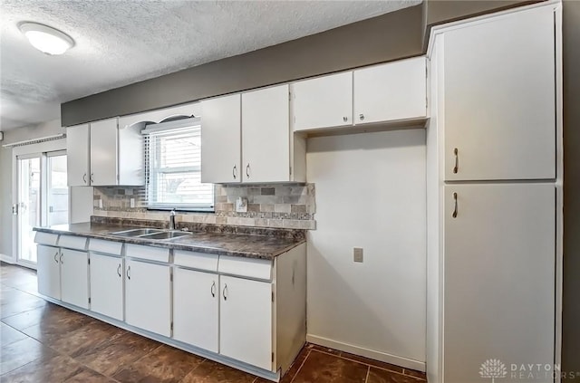 kitchen featuring dark countertops, white cabinetry, decorative backsplash, a textured ceiling, and a sink