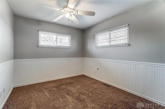 carpeted spare room with visible vents, a wainscoted wall, and a ceiling fan