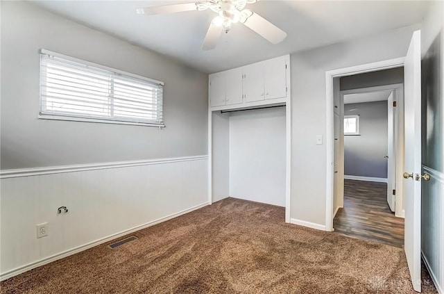 unfurnished bedroom featuring visible vents, a wainscoted wall, a closet, dark colored carpet, and ceiling fan