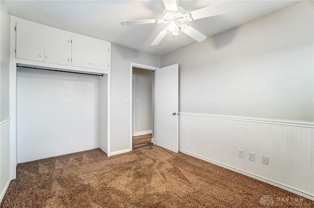 unfurnished bedroom featuring a closet, carpet flooring, ceiling fan, and a wainscoted wall