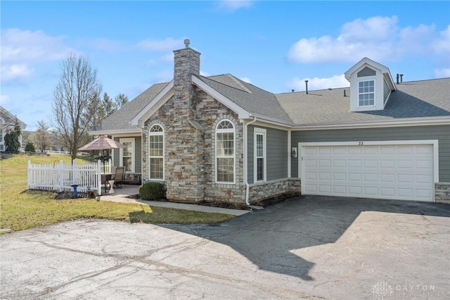 view of front of property with an attached garage, a shingled roof, a chimney, stone siding, and driveway