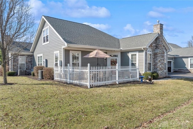 rear view of property featuring a yard, stone siding, roof with shingles, and a chimney