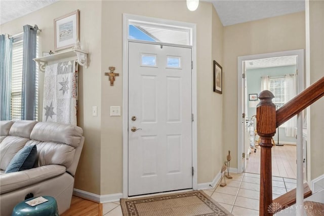 foyer entrance featuring stairway, light tile patterned floors, and baseboards