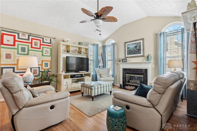 living area with a ceiling fan, wood finished floors, lofted ceiling, a fireplace, and a textured ceiling