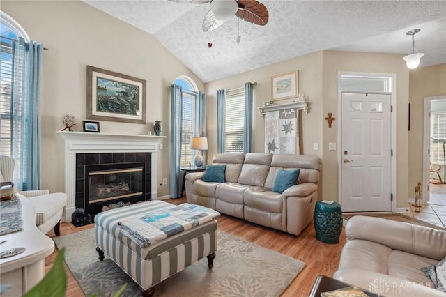 living room with a ceiling fan, a textured ceiling, wood finished floors, lofted ceiling, and a tile fireplace