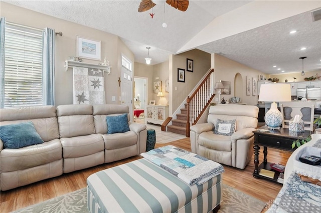 living room featuring arched walkways, stairway, light wood-style floors, and a wealth of natural light