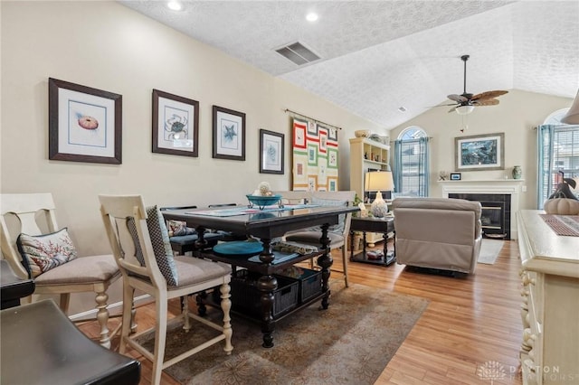 dining room featuring a ceiling fan, visible vents, light wood finished floors, vaulted ceiling, and a textured ceiling