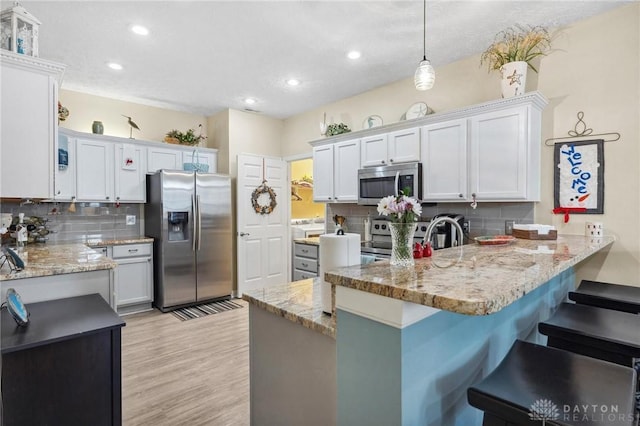 kitchen with backsplash, a breakfast bar, light wood-type flooring, appliances with stainless steel finishes, and a peninsula