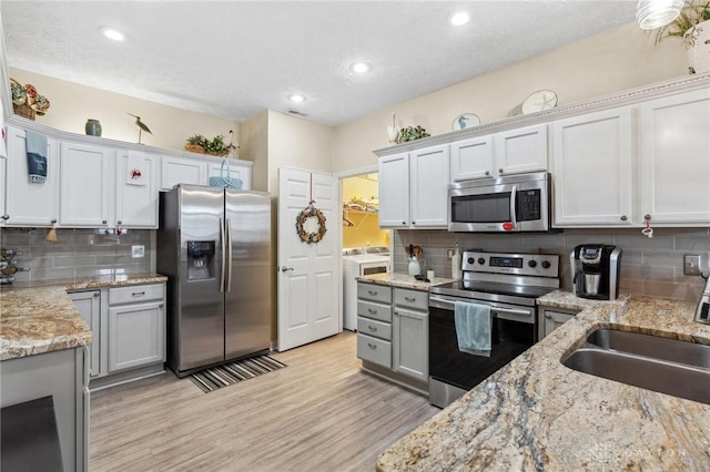 kitchen featuring washing machine and clothes dryer, tasteful backsplash, light wood-style flooring, appliances with stainless steel finishes, and a sink