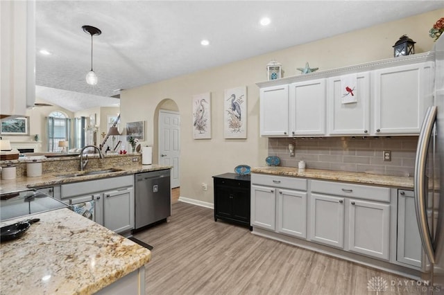 kitchen with light wood finished floors, tasteful backsplash, arched walkways, stainless steel appliances, and a sink