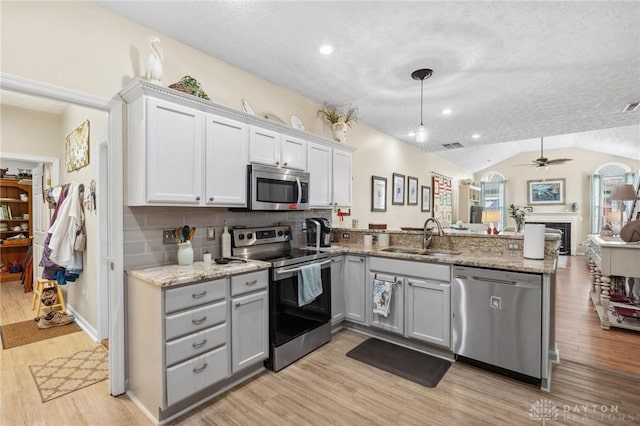 kitchen with a peninsula, light wood-style flooring, ceiling fan, a sink, and appliances with stainless steel finishes