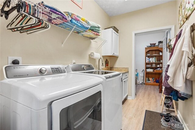 clothes washing area with cabinet space, washing machine and dryer, light wood-type flooring, and baseboards