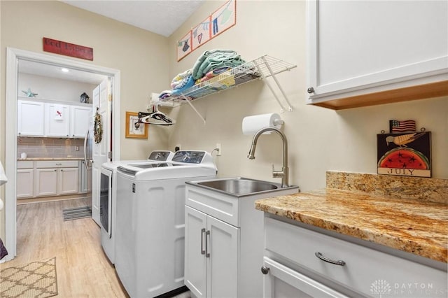 laundry room featuring light wood finished floors, washing machine and dryer, cabinet space, and a sink