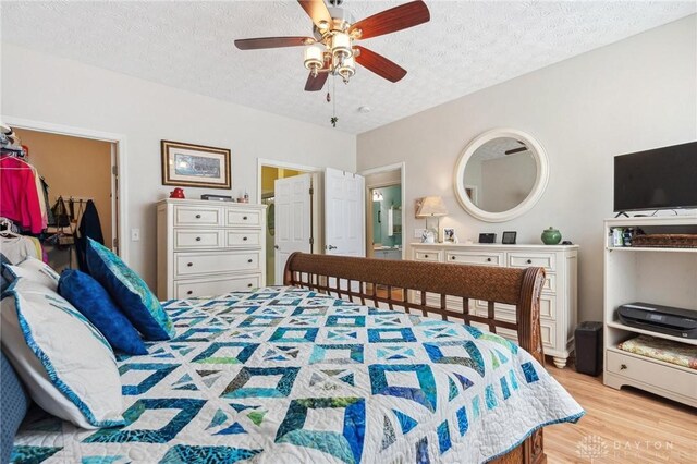 bedroom with a spacious closet, light wood-style flooring, a textured ceiling, and ceiling fan