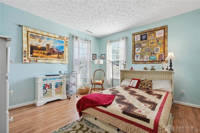 bedroom featuring baseboards, a textured ceiling, and wood finished floors