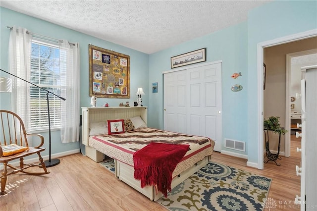 bedroom with visible vents, a textured ceiling, wood finished floors, a closet, and baseboards