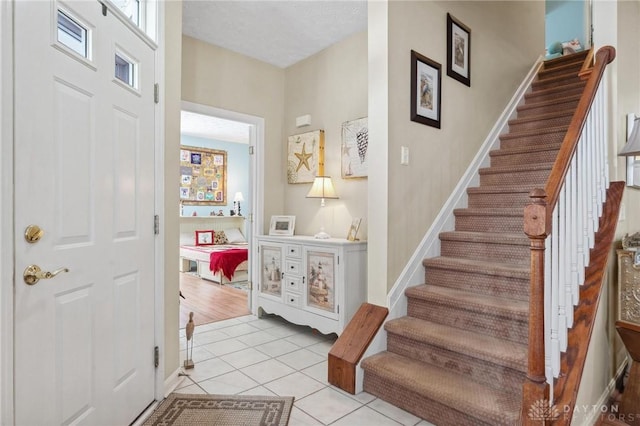 foyer featuring stairway, light tile patterned flooring, and baseboards