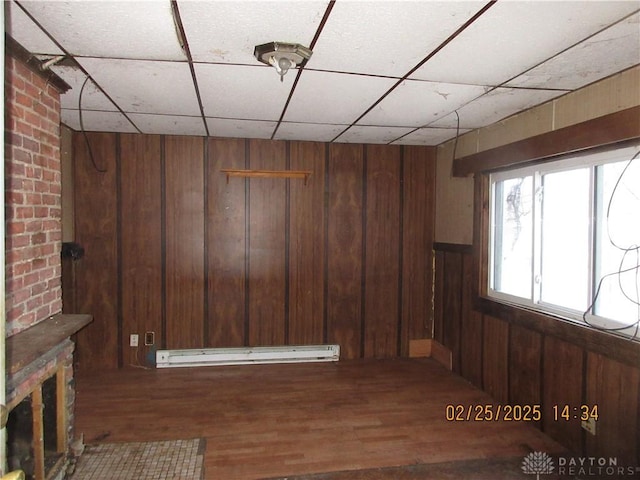 below grade area featuring baseboard heating, a drop ceiling, wood finished floors, and wood walls