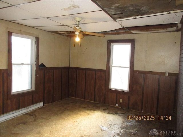 empty room featuring ceiling fan, a healthy amount of sunlight, wood walls, and wainscoting